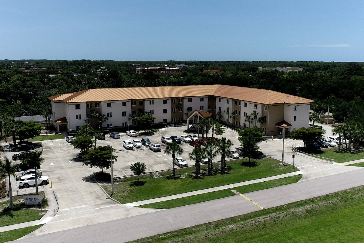 St. John XXIII Villas with large parking lot and palm trees